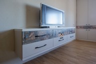 "Парящая" ТВ-тумба с выдвижными ящиками также украшена цветной полосой и достаточно вместительна