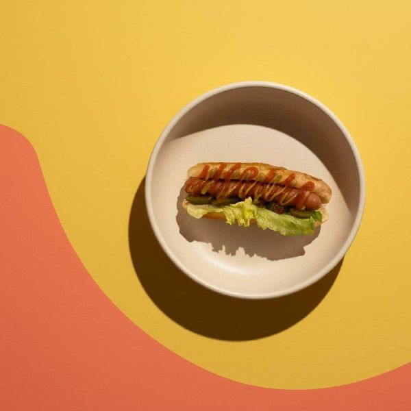 Концептуальная фуд-фотография стрит-фуда: хот-дог на желто-оранжевом фоне (color blocking). Яркая подача для меню