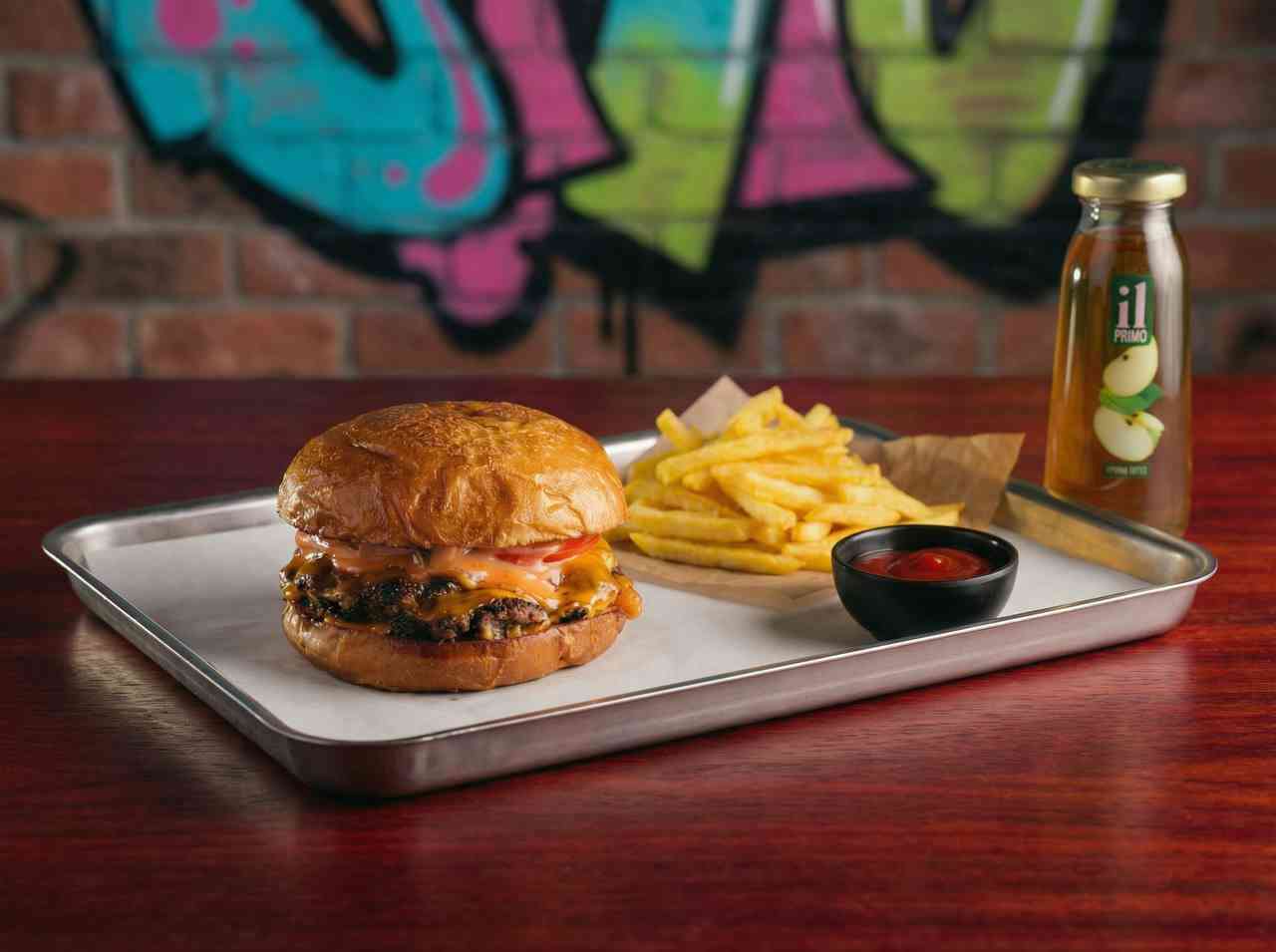 Рекламная фуд-фотография комбо-набора: крафтовый бургер, картофель фри и сок. Съемка стрит-фуда на металлическом подносе фоне граффити