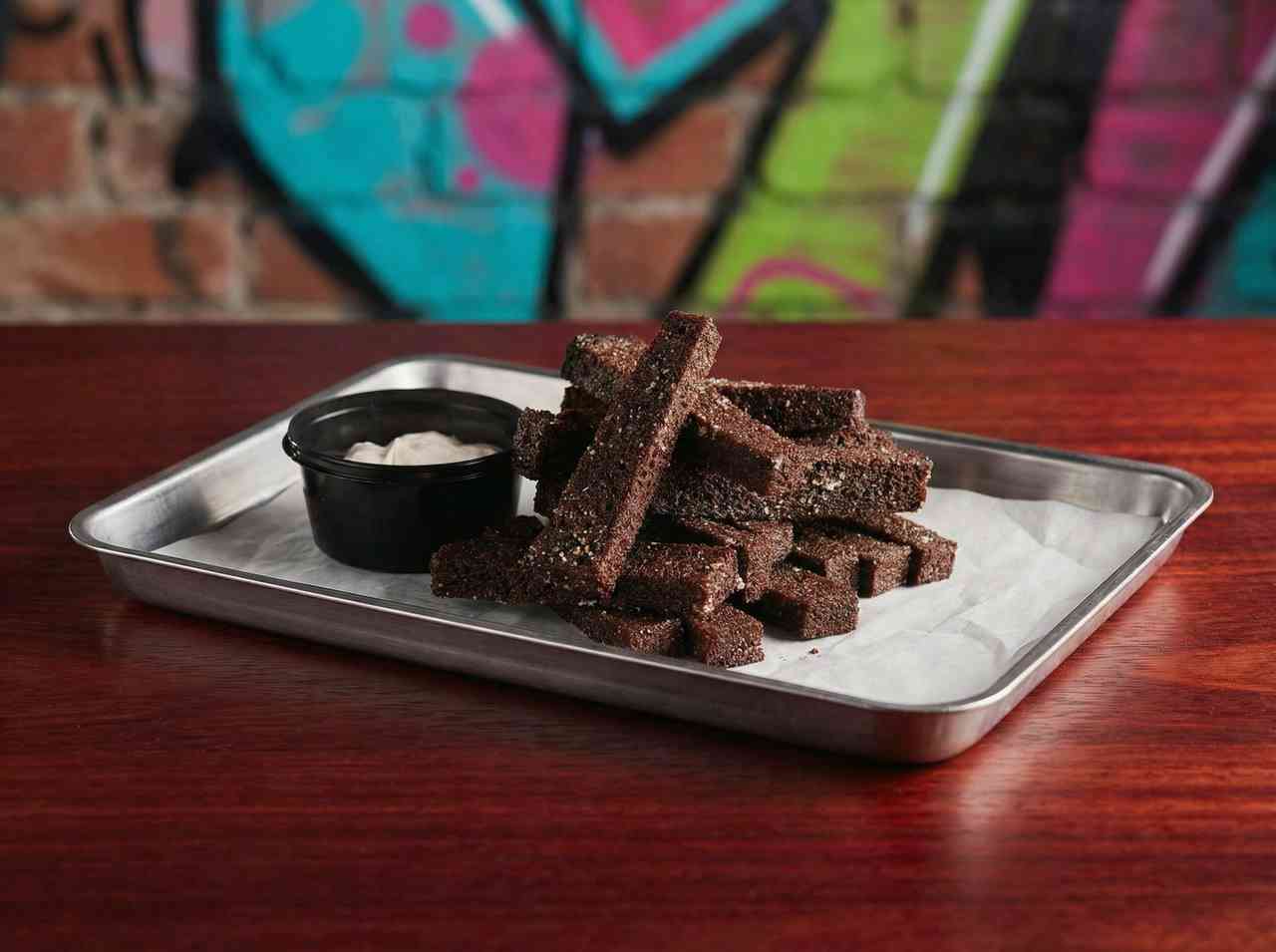 Съемка пивных закусок: чесночные гренки из черного хлеба с соусом на металлическом подносе. Атмосферное фото для молодежного бара