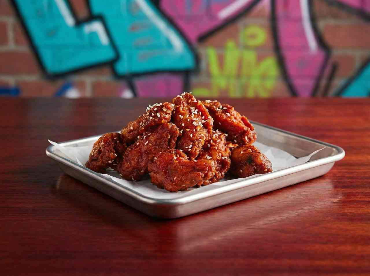 Аппетитная фуд-фотография куриных крылышек BBQ с кунжутом. Яркая предметная съемка стрит-фуда на фоне граффити