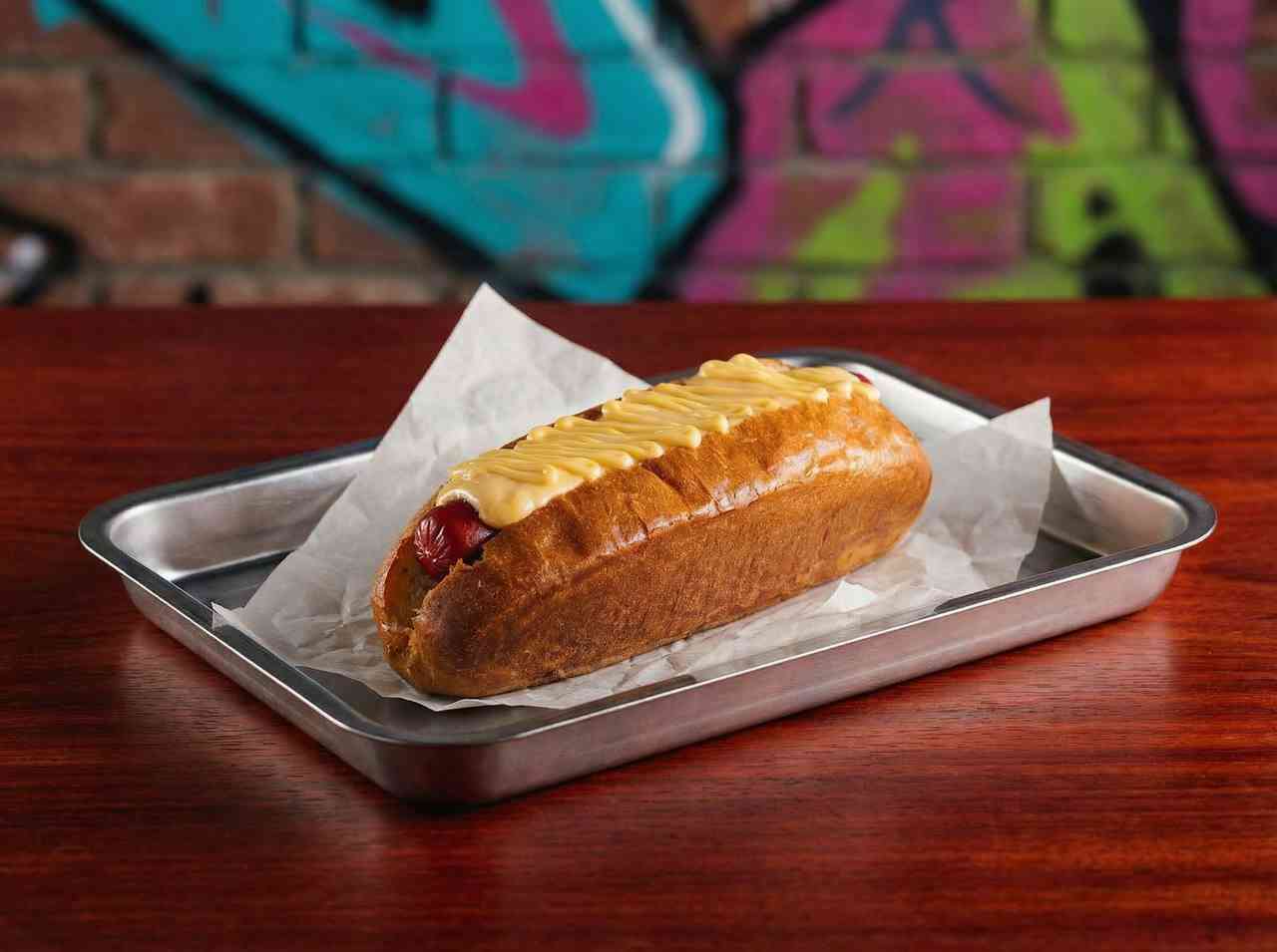 Рекламная фуд-съемка аппетитного хот-дога с сырным соусом. Профессиональное фото фаст-фуда в урбанистическом стиле