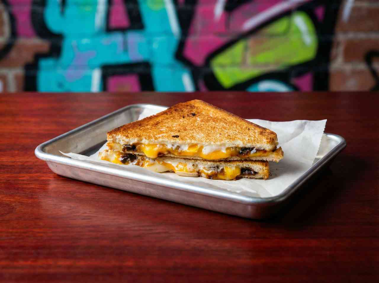 Аппетитная фуд-фотография горячего сэндвича с тянущимся сыром на металлическом подносе. Съемка уличной еды для агрегаторов доставки