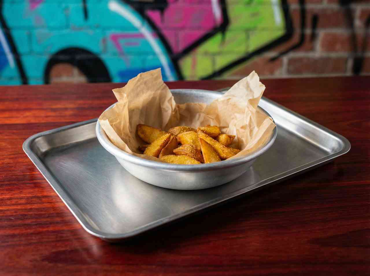 Предметная фуд-съемка картофеля по-деревенски в металлической миске. Обновление визуального стиля меню для молодежного кафе