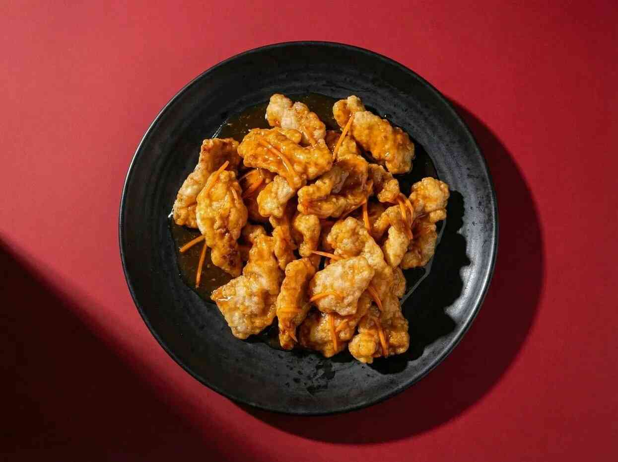 Профессиональная фуд-фотография мяса в кисло-сладком соусе, вид блюда сверху. Креативная съемка паназиатской кухни на красном фоне