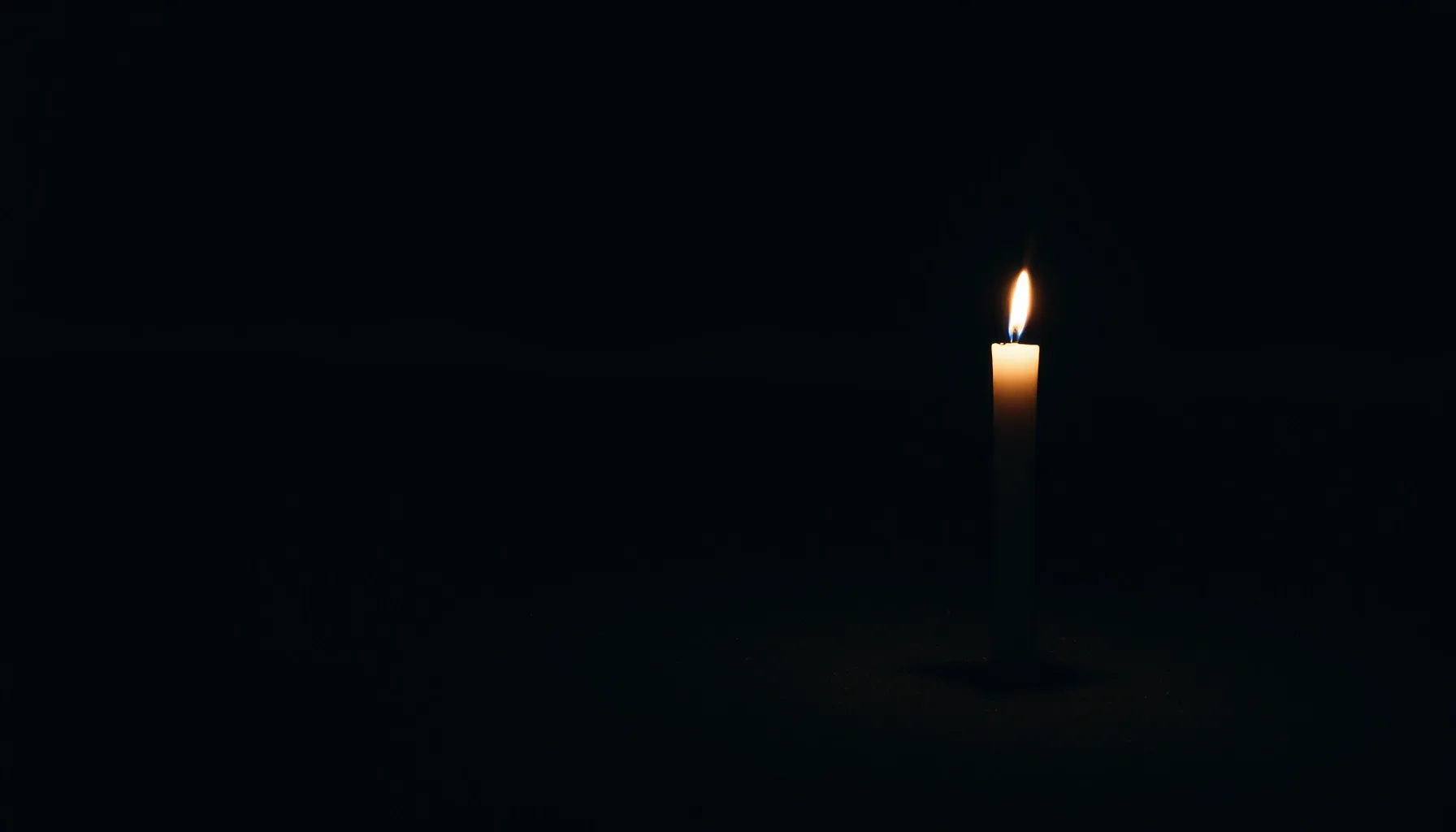 A lone candle standing on a dark sandy beach at night, refle...