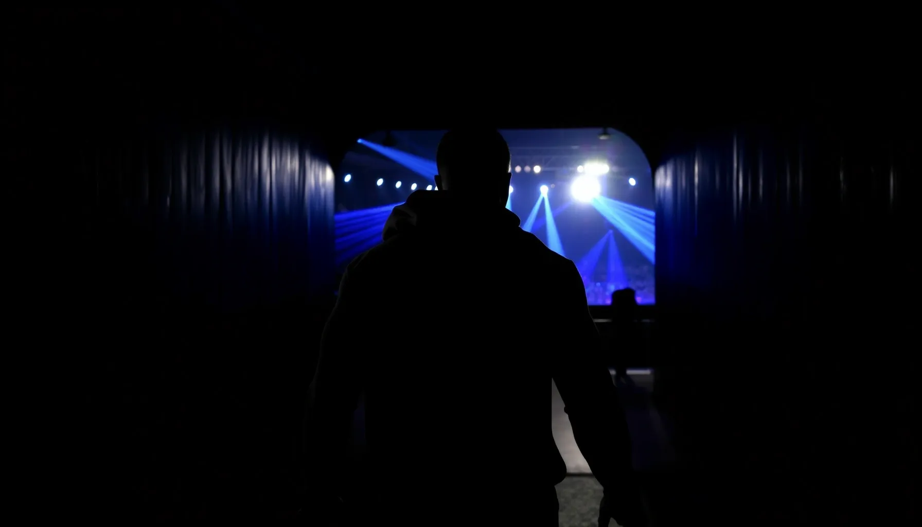 A muscular silhouette of a fighter in a hoodie walking throu...