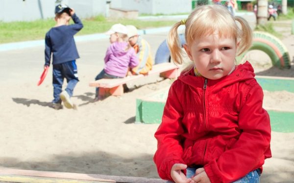 Девочка сидит одна у песочницы