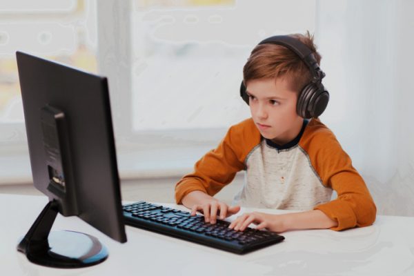Мальчик в наушниках играет в компьютерную игру