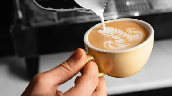 close-up-hand-pouring-milk-coffee-cup_23-2148865584-v1