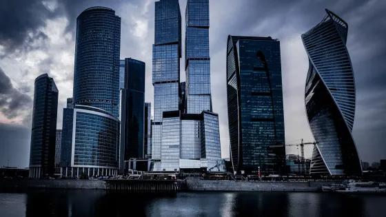 low-angle-shot-grey-skyscrapers-front-river-dark-cloudy-sky