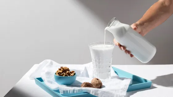 person-pouring-milk-full-glass-with-walnuts-tray_23-2148667729