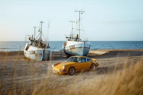 Yellow Porsche 911 against the backdrop of old fishing boats by the sea