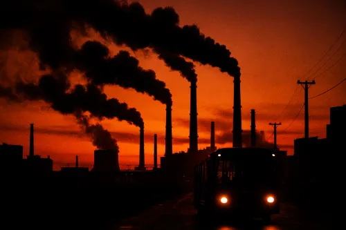 Silueta de chimeneas industriales contra un brillante atardecer con humo