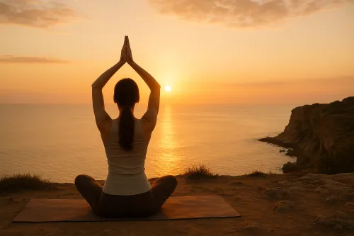 Mujer en posición de meditación mirando el atardecer junto al océano