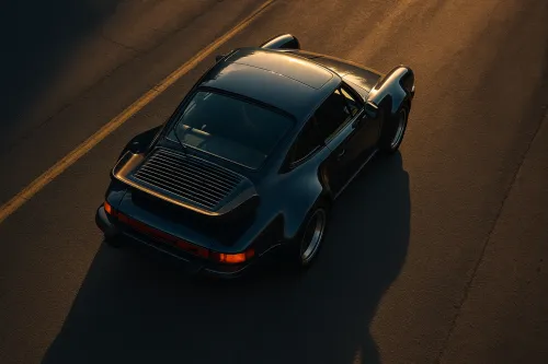 View of a black sports car from above, set against the road in the golden light of sunset