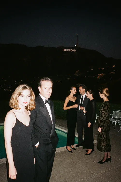 Grupos de personas en un evento nocturno en la piscina con vista al letrero de Hollywood