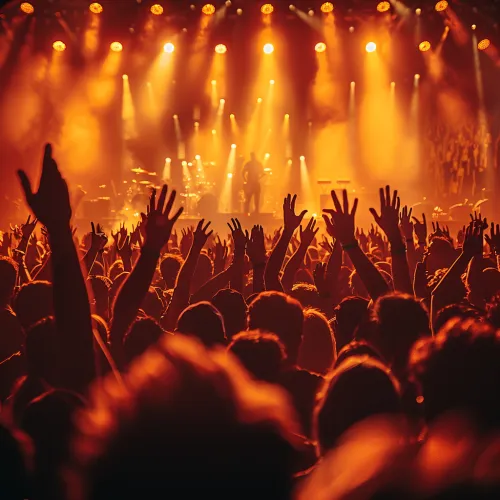 Audience at a concert under bright lights, raising their hands in excitement