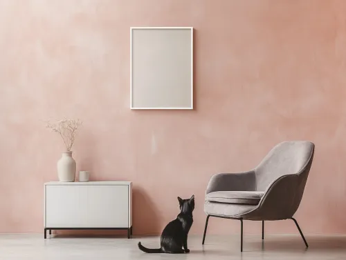 Sillón cómodo y gato frente a un cuadro vacío en la pared rosa