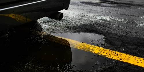 Black car and its exhaust on a wet road with a yellow line
