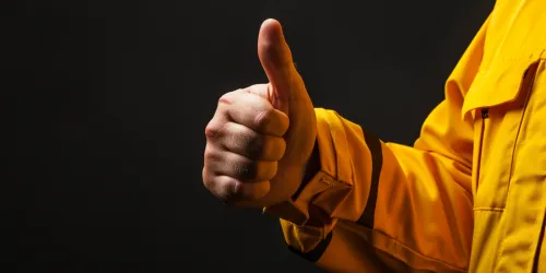 Mano con el pulgar levantado sobre un fondo negro en una chaqueta amarilla