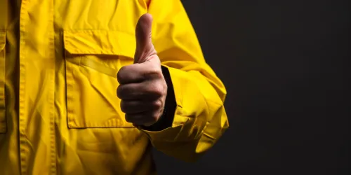 Persona en una chaqueta amarilla mostrando el gesto 'thumbs up' sobre un fondo negro