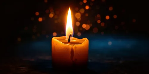 Candle with a burning wick and gentle flames around it against a dark backdrop
