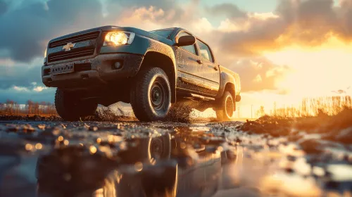 Black Chevrolet pickup truck splashing through muddy road during sunset