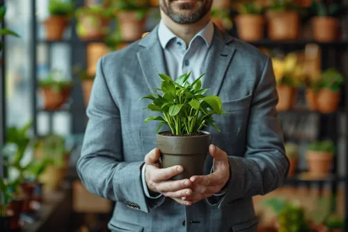 A man in a business suit holding a green pot with a plant