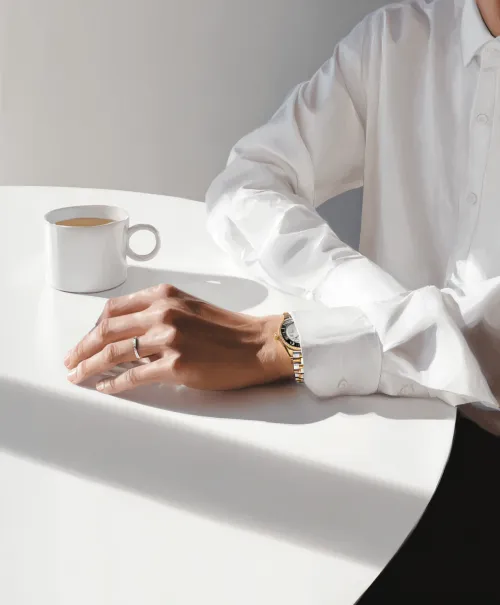 Hand in a white shirt holding a cup of coffee on the table
