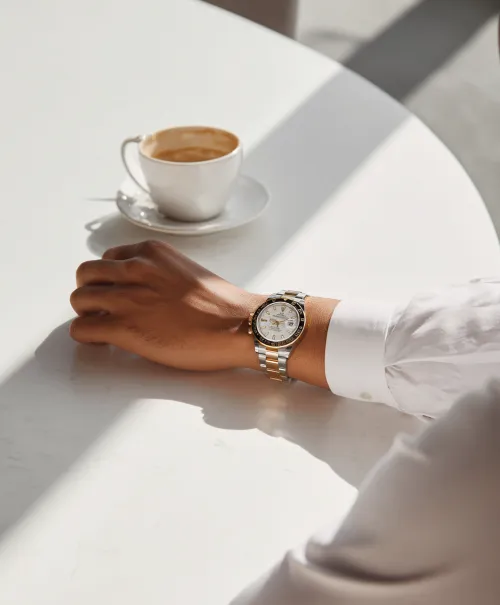 Stylish wristwatch on a hand with a cup of coffee on the table