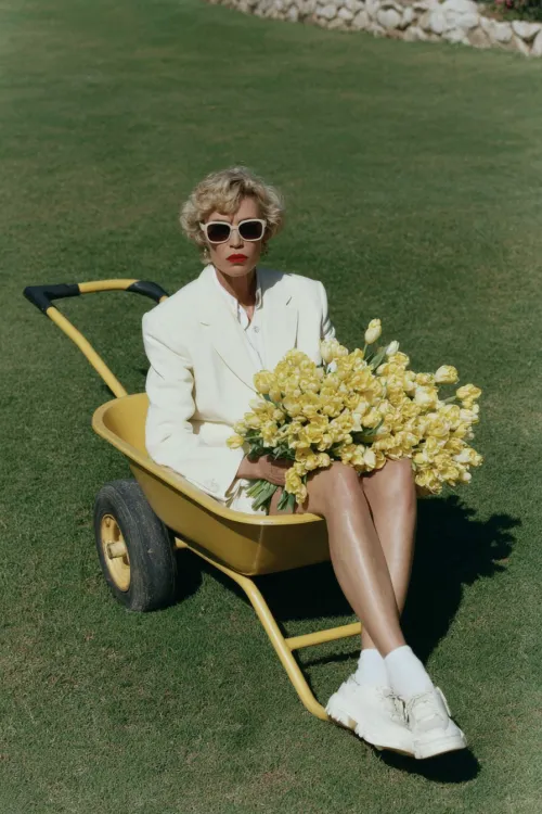 Stylish woman in a white suit and sunglasses with flowers on the lawn