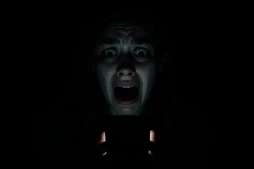 A woman with a scared expression looks at the phone screen in the dark