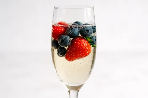 Стеклянный бокал с шампанским, клубникой и голубикой