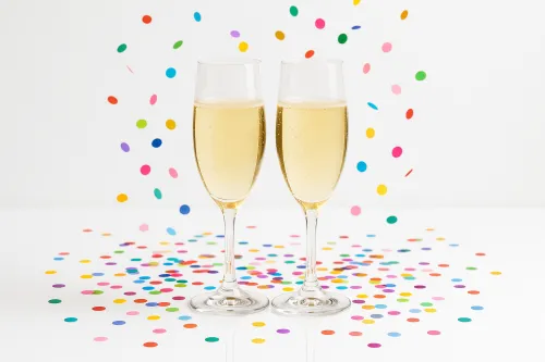 Два бокала шампанского среди конфетти на белом фоне