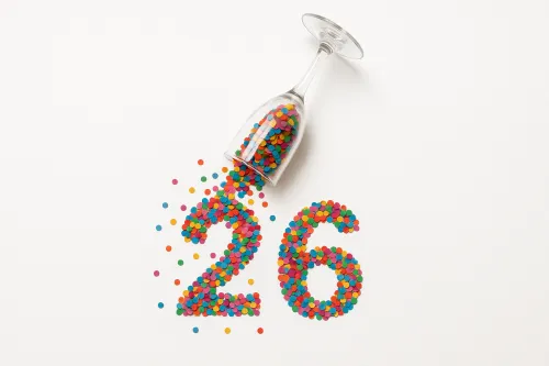 Стеклянный бокал с цветными конфетти, образующими числа 26