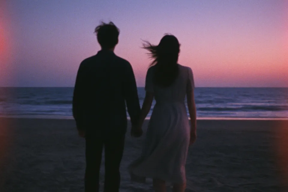 Una pareja tomados de la mano, caminando por la playa al atardecer