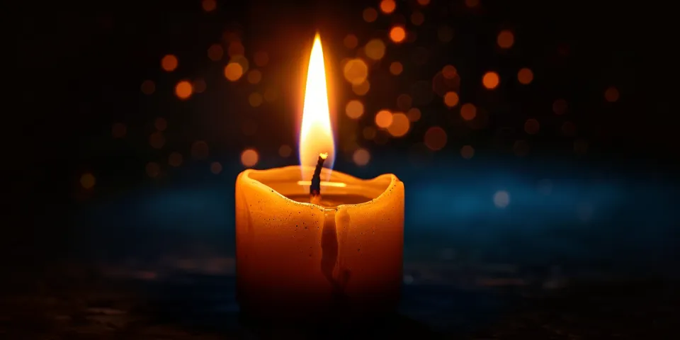 Vela con una mecha ardiente y suaves luces alrededor sobre un fondo de oscuridad