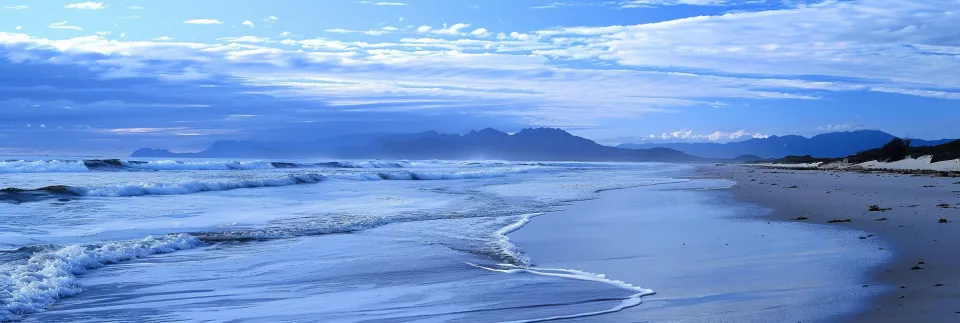 Seaside with Waves and Clouds Against a Mountain Background