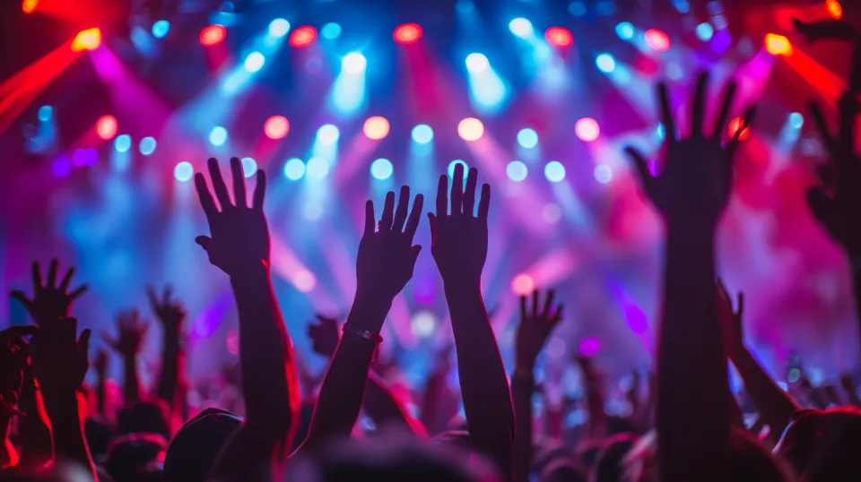 Concert atmosphere with raised hands of spectators against a backdrop of bright lights