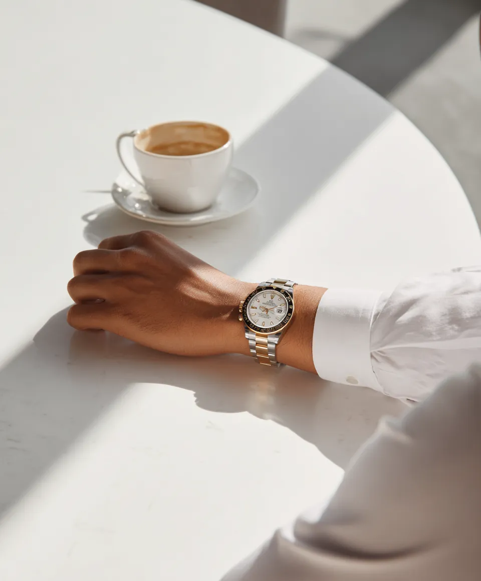 Stylish wristwatch on a hand with a cup of coffee on the table