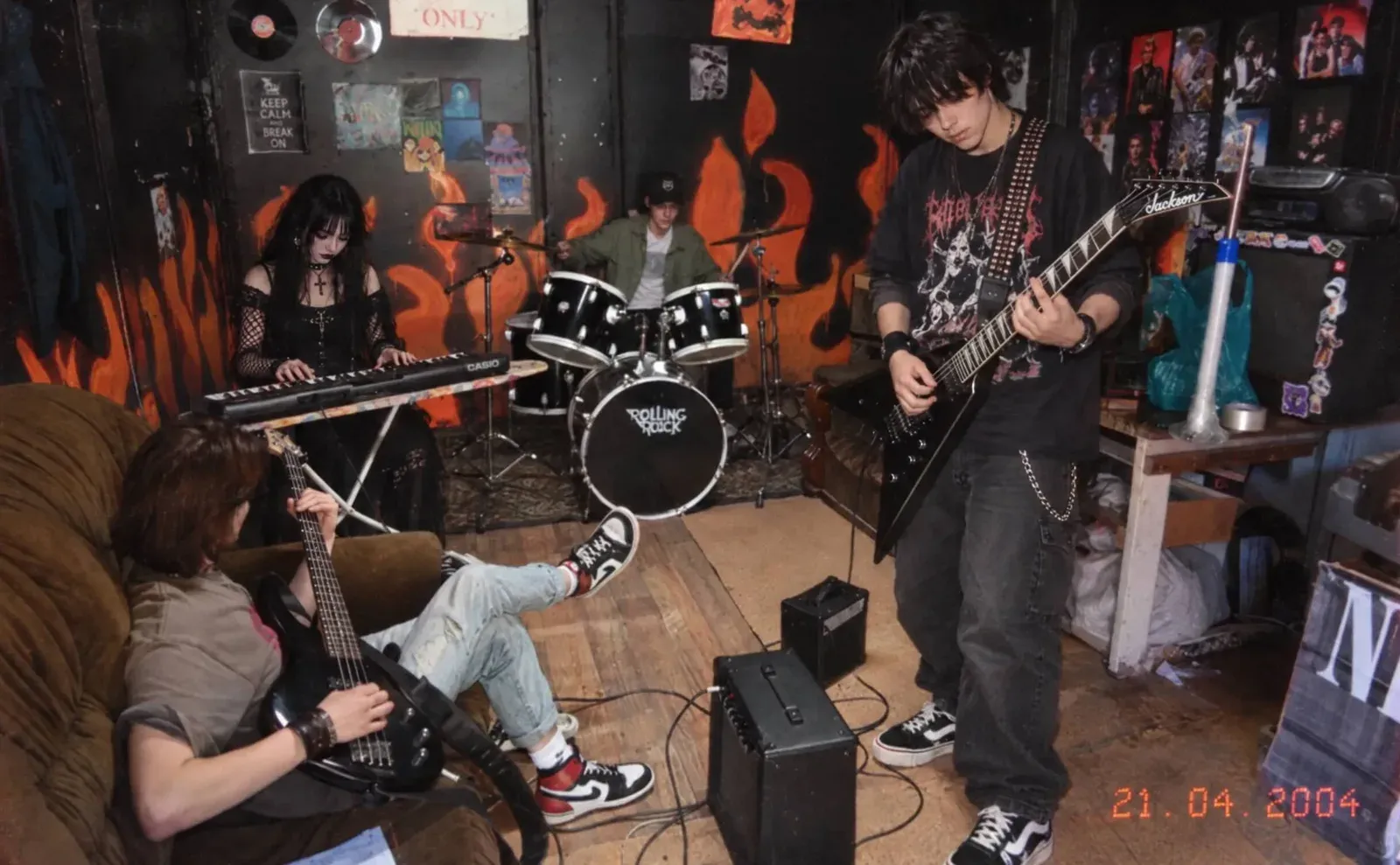 A garage rehearsal: drums, bass, a Casio keyboard and a guitar among amps and posters on the walls