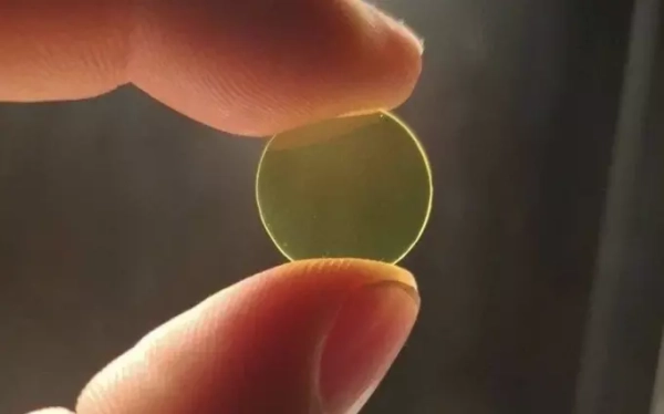 Пальцы держат прозрачный круглый желтый объект против света.