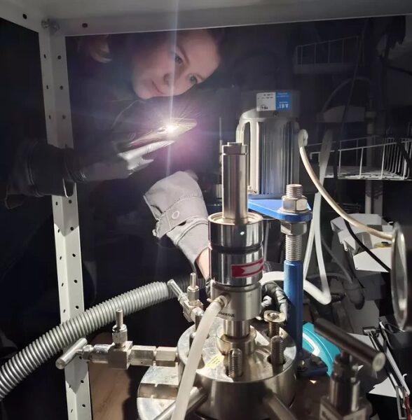 Химики нашли способ продлить срок службы литий-ионных аккумуляторов 1 Человек с фонариком изучает оборудование в лаборатории. Блестящие металлические трубы.