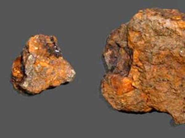 Два куска иридия на сером фоне: крупный и мелкий, яркого оранжево-коричневого цвета.