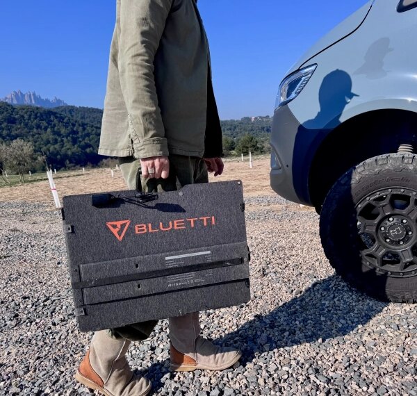 Человек с портативной солнечной панелью Bluetti рядом с автомобилем на открытом воздухе.