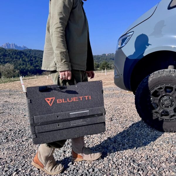 Человек с портативной солнечной панелью Bluetti рядом с автомобилем на открытом воздухе.