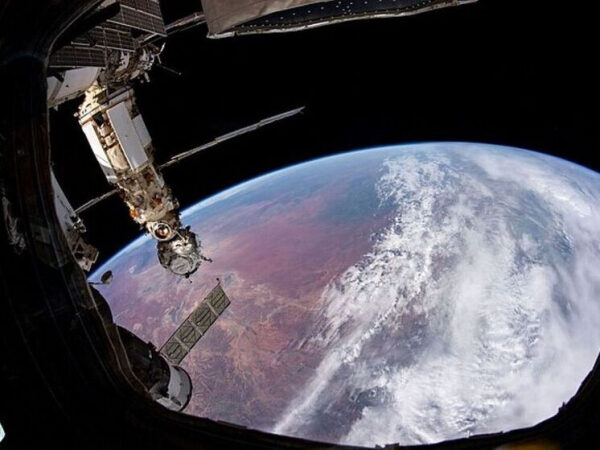 Вид Земли из космоса с МКС, облака над континентом, космическая станция на переднем плане.