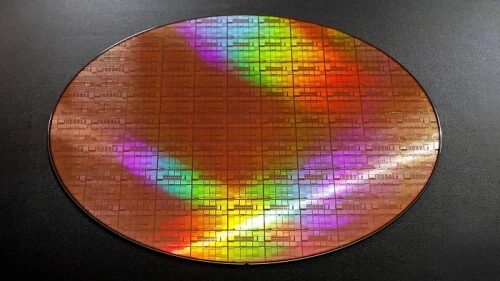 Кремниевая пластина с микрочипами, переливающаяся яркими цветами на черном фоне.