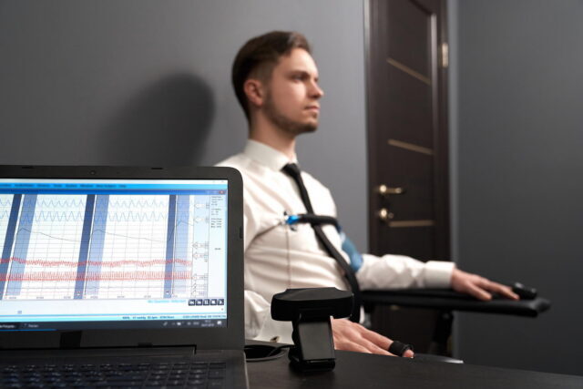 Мужчина проходит тест на детекторе лжи в офисе. На переднем плане ноутбук с графиками.